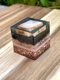 a glass cube with black, brown, and white sand