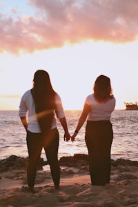 two women holding hands on the beach at sunset