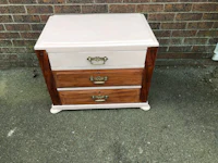 a pink nightstand with two drawers in front of a brick wall