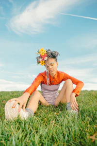 a woman sitting in the grass with flowers in her hair