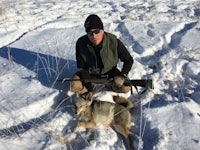 a man kneeling next to a dead coyote in the snow