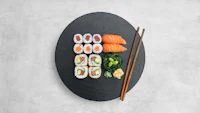 japanese sushi on a black plate with chopsticks