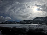 the sun shines over a snow covered field and mountains
