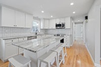 a kitchen with white cabinets and marble counter tops