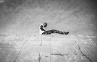 a black and white photo of a man sitting on a concrete wall