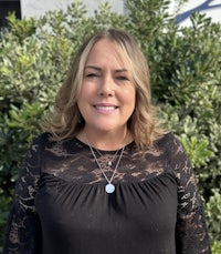 a woman wearing a black lace top standing in front of bushes