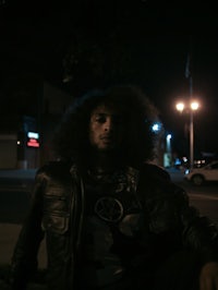 a man with curly hair sitting on a sidewalk at night