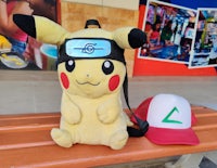 a stuffed pikachu sits on a bench next to a hat