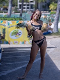 a woman in a black bikini holding pineapples