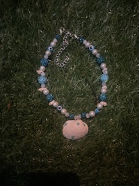a necklace with a blue and white shell laying on the grass