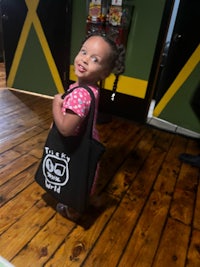 a little girl holding a black tote bag