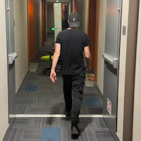 a man walking down a hallway in a black hat