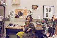a woman sitting at a desk in a messy room