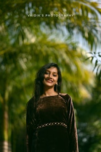 a woman in a brown dress standing in front of a palm tree