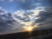 the sun is setting over a highway with clouds in the background