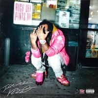 a man in a pink shirt is crouching on the sidewalk