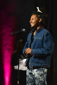 a man in a denim jacket is smiling into a microphone