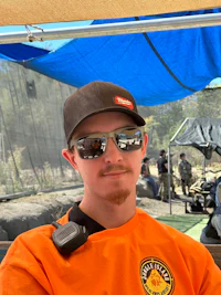 a man wearing sunglasses and an orange shirt sitting under a tent
