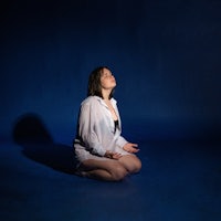 a woman sitting on the floor in front of a blue background