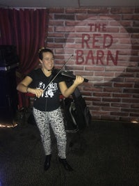 a woman playing violin in front of a red barn sign