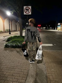 a man holding a shopping bag on a sidewalk at night