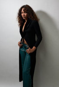 a woman in black and green pants posing in front of a white wall