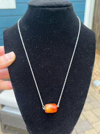 a person is holding an orange stone necklace on a mannequin