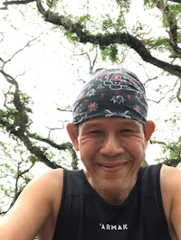 a man wearing a hat and a bandana in front of a tree