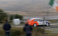 a rally car driving down a road with irish flags in the background