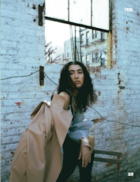 a woman is sitting on a bench in front of a brick wall