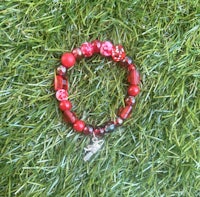 a bracelet with red beads and a charm on the grass