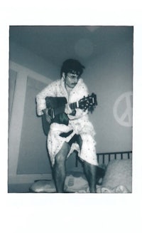 a black and white photo of a man playing guitar on a bed