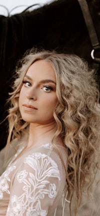 a woman with long curly hair is posing next to a horse