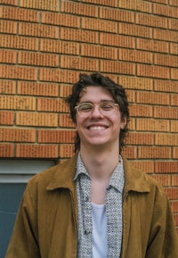 a young man smiling in front of a brick wall
