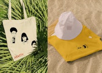 a hat, t - shirt and a tote bag on the sand