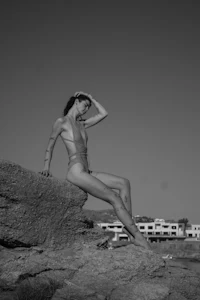 a woman in a bikini sitting on a rock