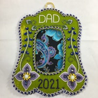 a green and purple ornament with the word dad 2021