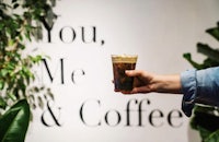 a person holding a cup of coffee in front of a sign that says you me & coffee