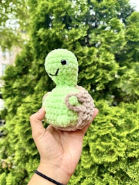a person holding a crocheted turtle in front of a tree