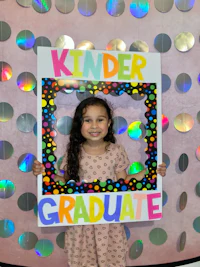 a little girl holding up a frame that says kinder graduate