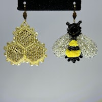 a pair of bee beaded earrings on a stand