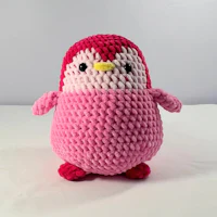 a crocheted pink penguin sitting on a white surface