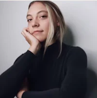 a woman in a black turtleneck shirt leaning against a wall