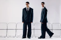 two men in suits standing in front of chairs