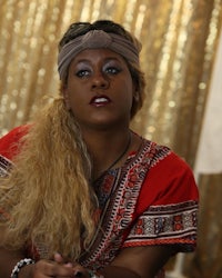 a woman with blond hair sitting in front of a gold background