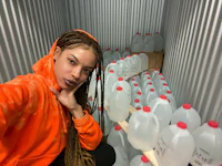 a woman in an orange hoodie posing in front of jugs of water