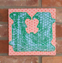 a green and pink polka dot tile hanging on a brick wall