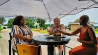 three women sitting at a table under an umbrella