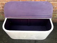 a purple and white trash can sitting on a brick wall
