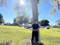 a boy leaning against a tree in a park